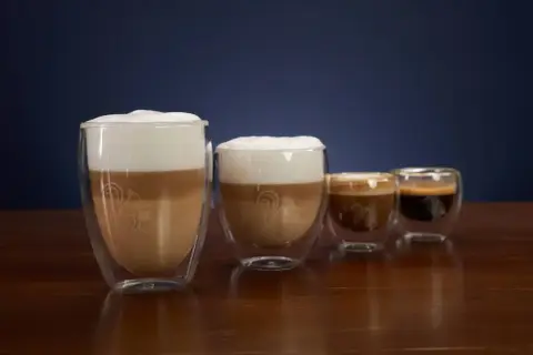 Vier Gläser mit Kaffee und Milchschaum. Das größte Glas zeigt, was ist milchkaffee: geschichtete Milch und Kaffee mit viel Schaum.