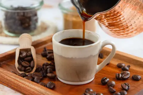 Frisch aufgebrühter türkischer Mokka fließt in eine Tasse. Kaffeebohnen liegen auf einem Holztablett.