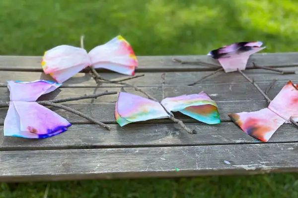 Bunte Schmetterlinge aus Kaffeefiltern, die Kinder leicht selber machen können, sitzen auf einem Holzbrett.
